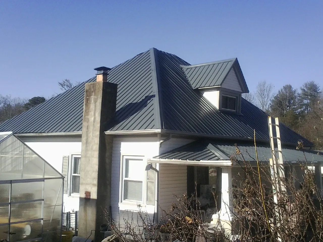 Dark blue standing seam metal roof on a white farmhouse with dormer — Slate & Tile Roof Repair by Roofing Brothers in Brush