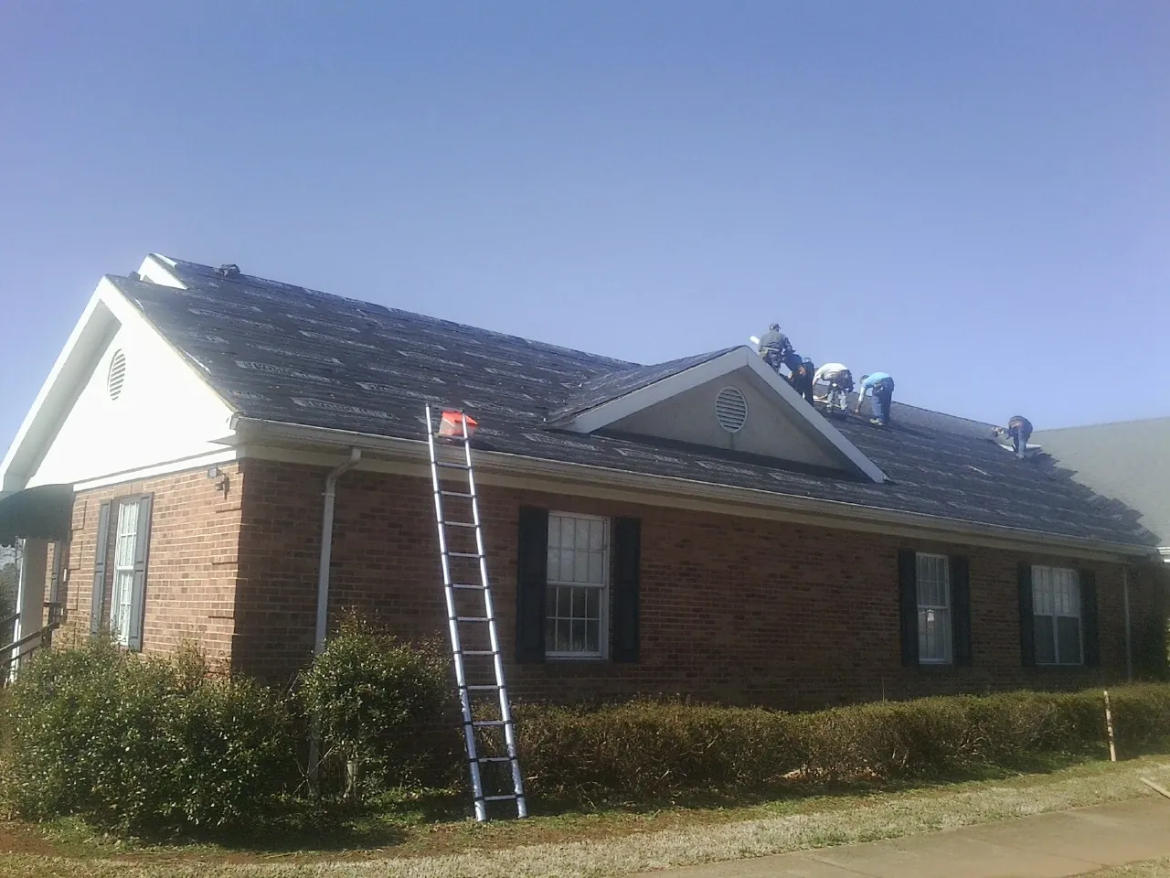 Crew tearing shingles off a brick ranch roof with a ladder set — Metal Roof Repair work by our crew in Brush