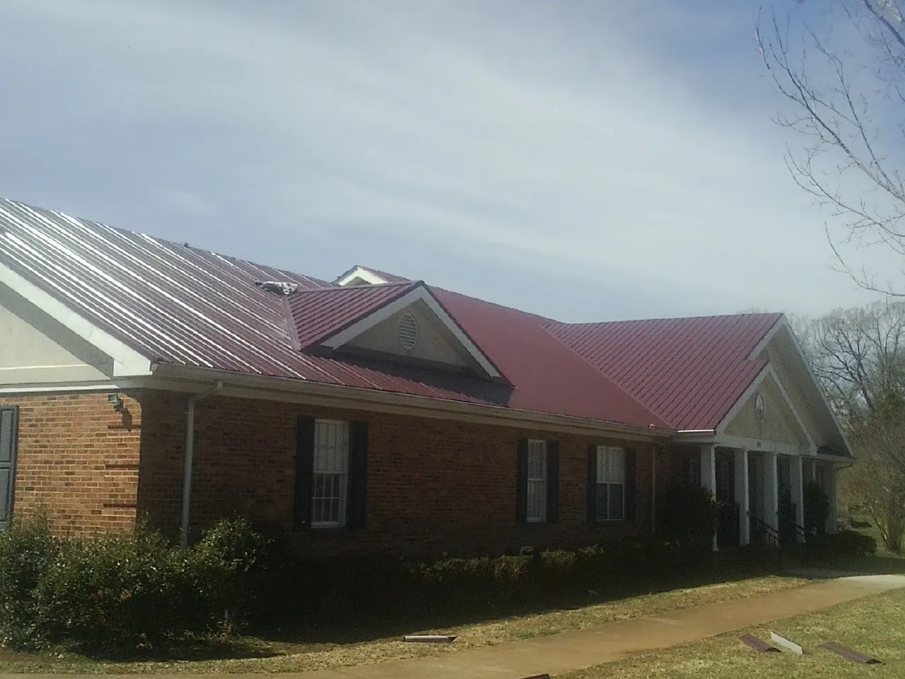 Red metal roof with gabled entries on a long brick building, from a Hail Damage Roof Repair job in Brush
