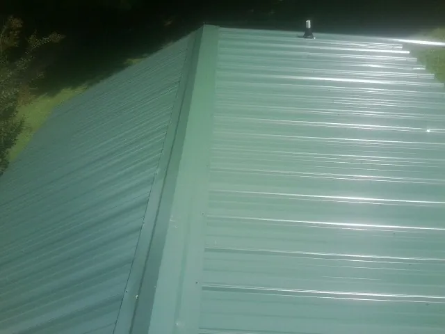 New green metal panels meeting at the ridge of a roof — Flat Roof Repair work by our crew in Brush