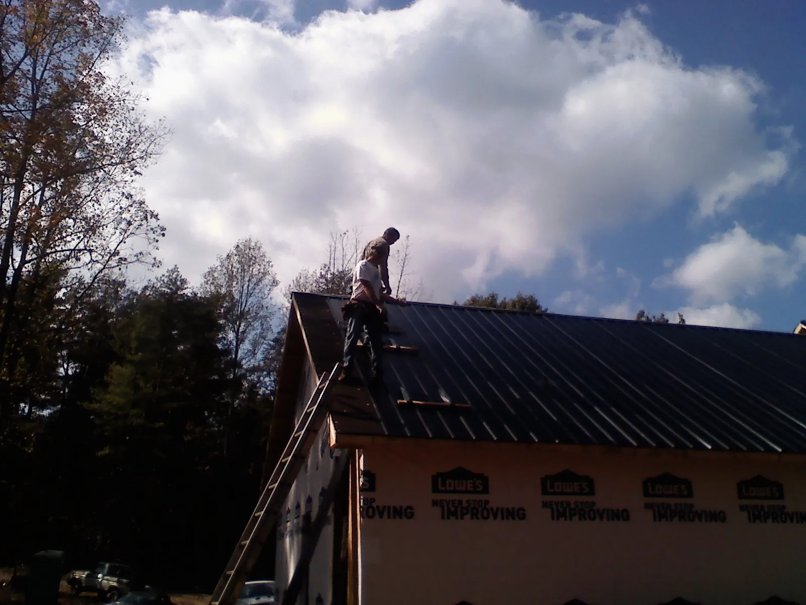 Roofer fastening dark metal panels high against a cloudy sky, from a Roof Inspection job in Brush