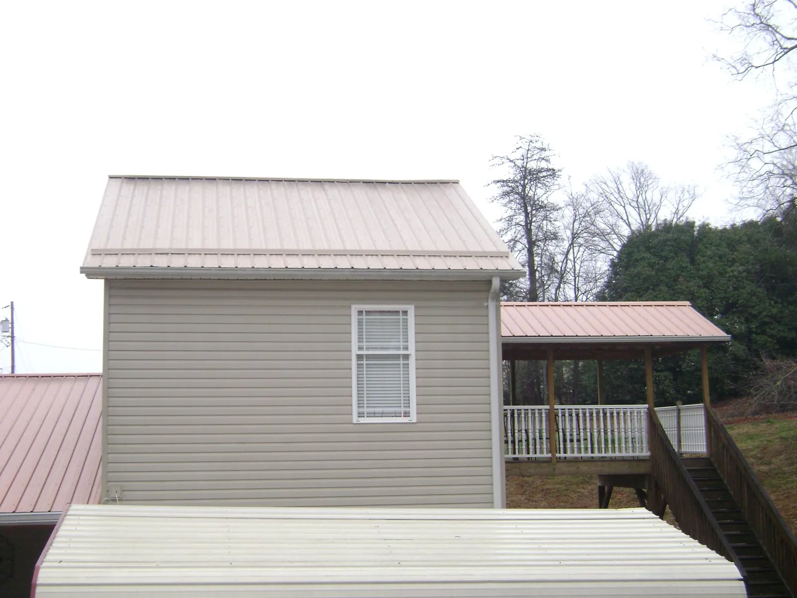 Tan metal roofs on a two story addition and attached porch, from a Roof Replacement job in Brush